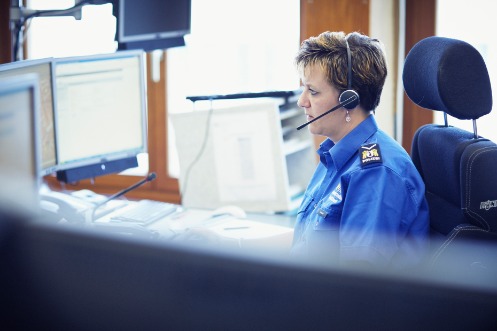 Polizistin mit Headset vor mehreren Bildschirmen in einer Anrufzentrale der Kantonspolizei Basel-Stadt.