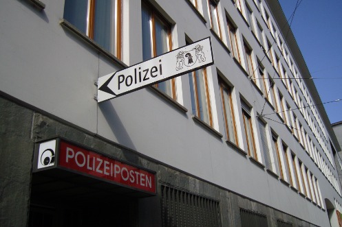 Gebäude des Polizeiposten Spiegelhof, der Fokus liegt auf dem Eingangsbereich. Ein rotes sowie ein weisses Schild mit der Aufschrift "Polizei" markieren den Zugang zum Gebäude. Die Fenster im Untergeschoss sind vergittert.