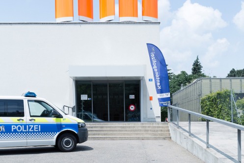 Eingangsbereich der Polizeiwache Kannenfeld mit automatischer Glasschiebetür. Ein blaues Banner mit der Aufschrift "Kantonspolizei" ziert den Zugang zum Polizeirevier. Vor der Wache parkt ein kleiner Polizeibus. 