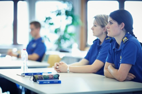 Zwei Polizeischülerinnen und ein Polizeischüler in einem Klassenzimmer, beim Unterricht im Zuge ihrer Ausbildung.