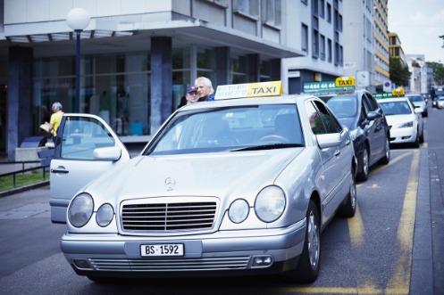 Silbernes Taxi der Marke Mercedes, mit offener Beifahrertür, an einem Taxistand im Kanton Basel-Stadt.